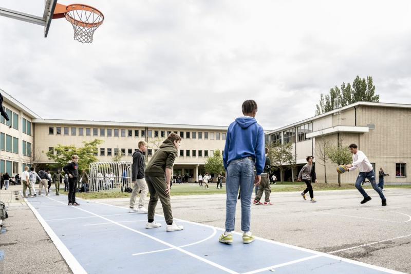 Een groepje leerlingen spelen basketbal op de speelplaats van Het Gymnasion.